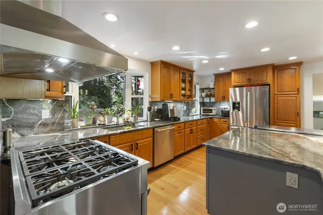 a kitchen with stainless steel appliances granite countertop a stove a sink dishwasher a refrigerator and white cabinets with wooden floor