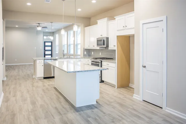 a kitchen with stainless steel appliances granite countertop a refrigerator a sink dishwasher and white cabinets with wooden floor