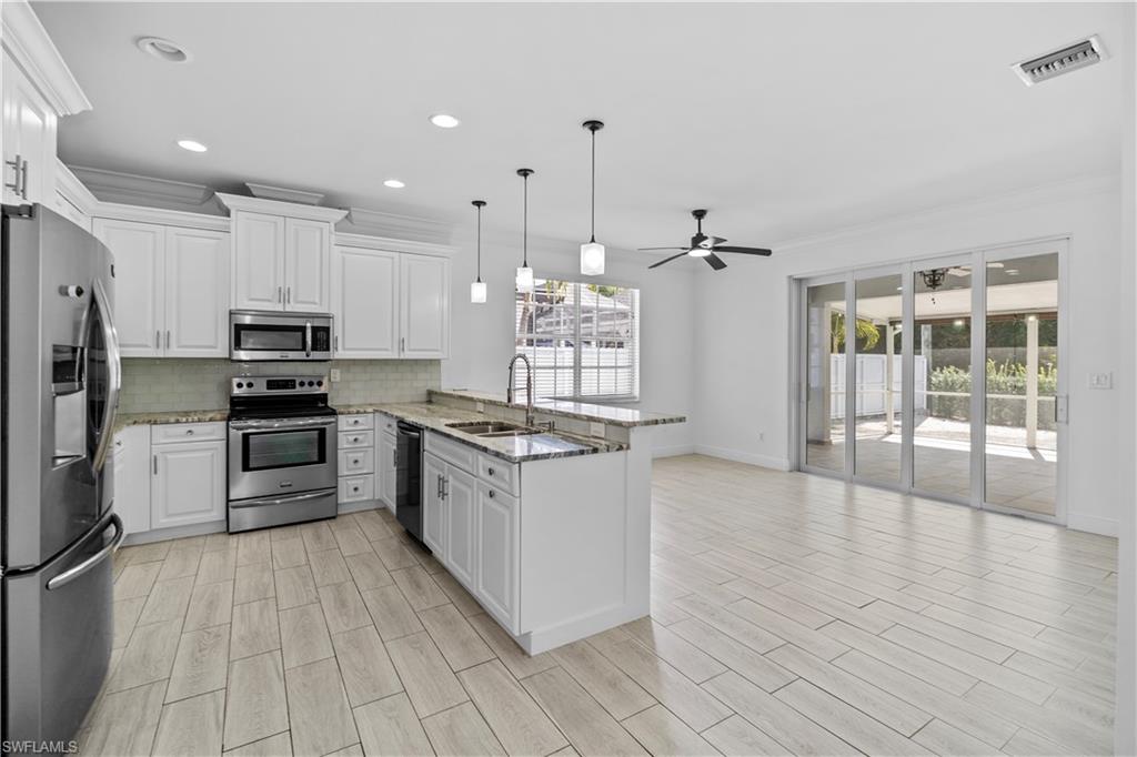 183 7th Street Naples, FL 34113 - Photo 9 of 50 a large kitchen with granite countertop a stove top oven a sink dishwasher a refrigerator and white cabinets with wooden floor