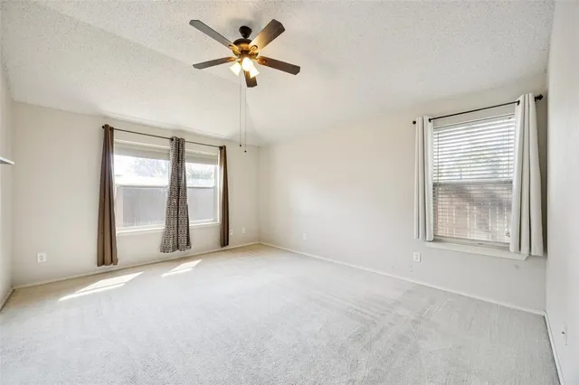 an empty room with chandelier fan and windows