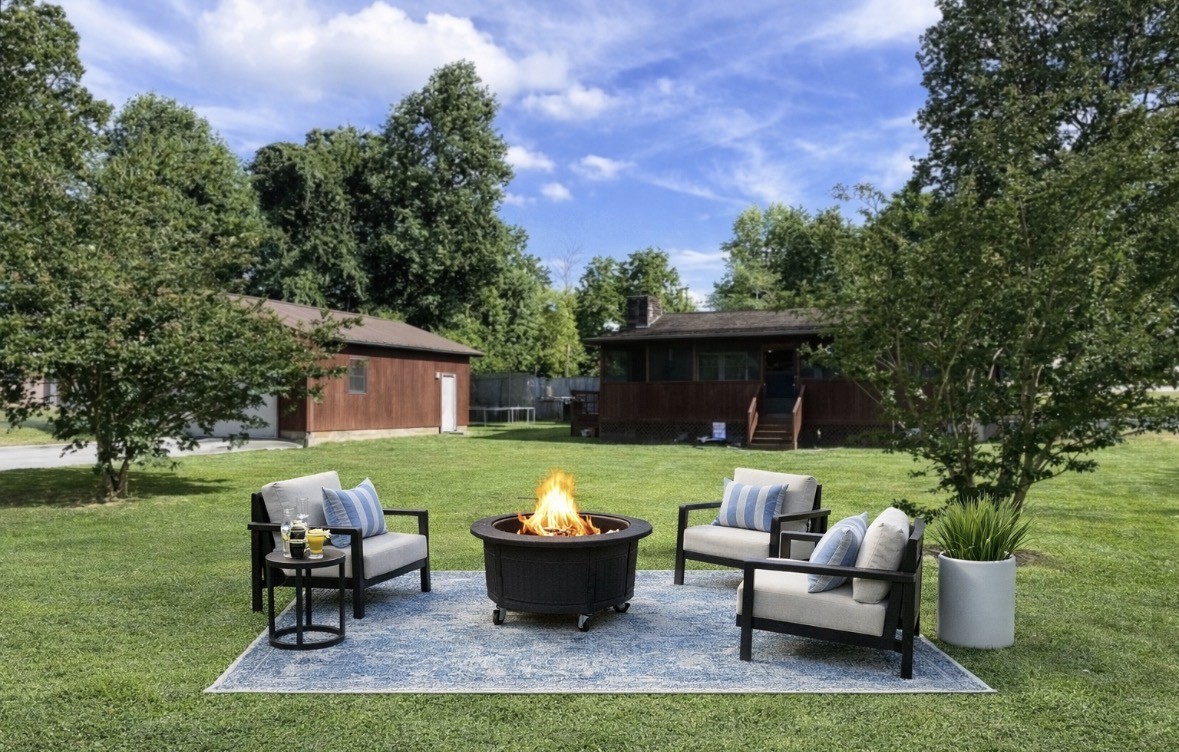 a view of a patio with couches chairs and a fire pit with large trees