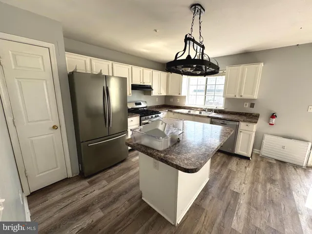 a kitchen with stainless steel appliances granite countertop a refrigerator a sink dishwasher a stove and white cabinets with wooden floor