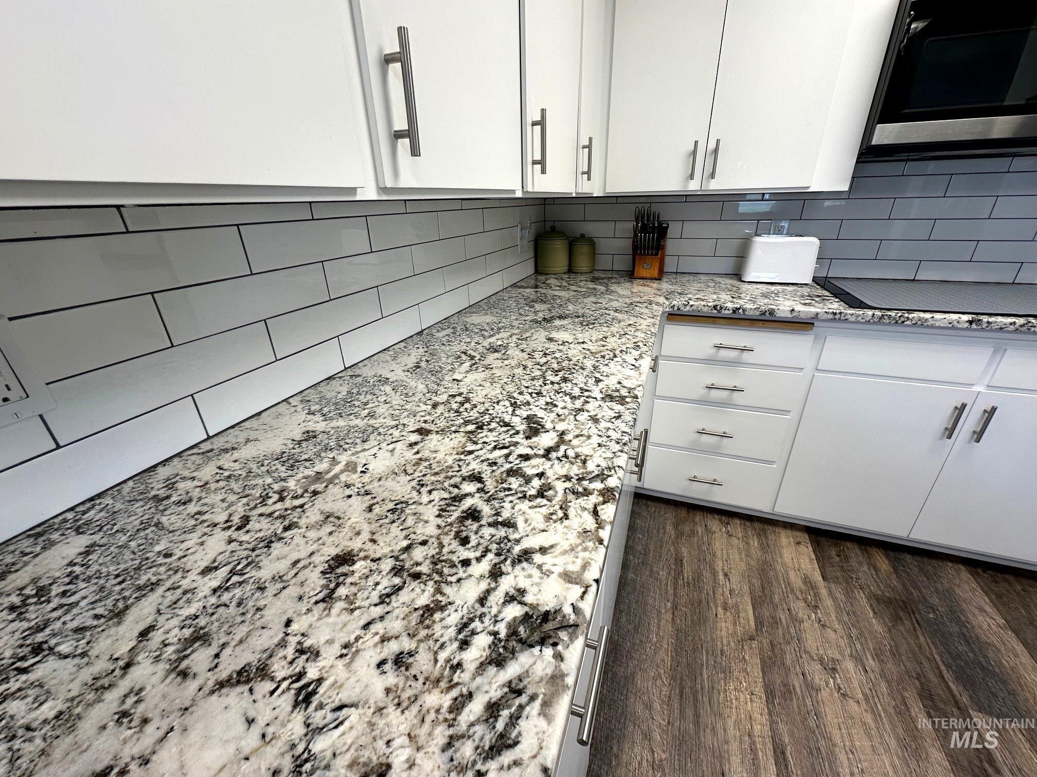 4436 Baker Road Ontario, OR 97914 - Photo 4 of 30 Kitchen featuring white cabinets, light stone countertops, dark wood-style flooring, decorative backsplash, and black electric cooktop