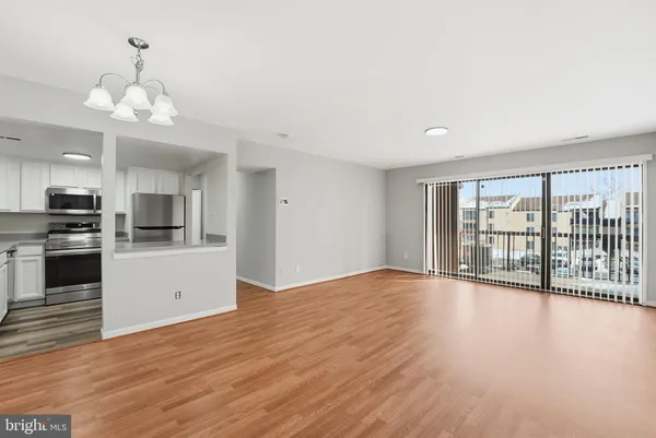 a view of an empty room with wooden floor and kitchen