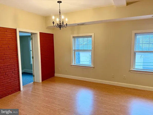 an empty room with wooden floor chandelier and windows