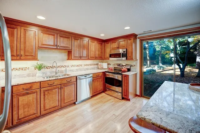 a kitchen with stainless steel appliances granite countertop a stove a sink dishwasher a microwave oven and a dining table with wooden cabinet