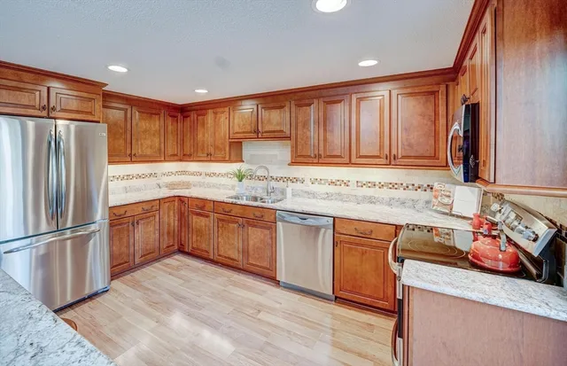 a kitchen with stainless steel appliances granite countertop a refrigerator a sink dishwasher and wooden cabinets with wooden floor