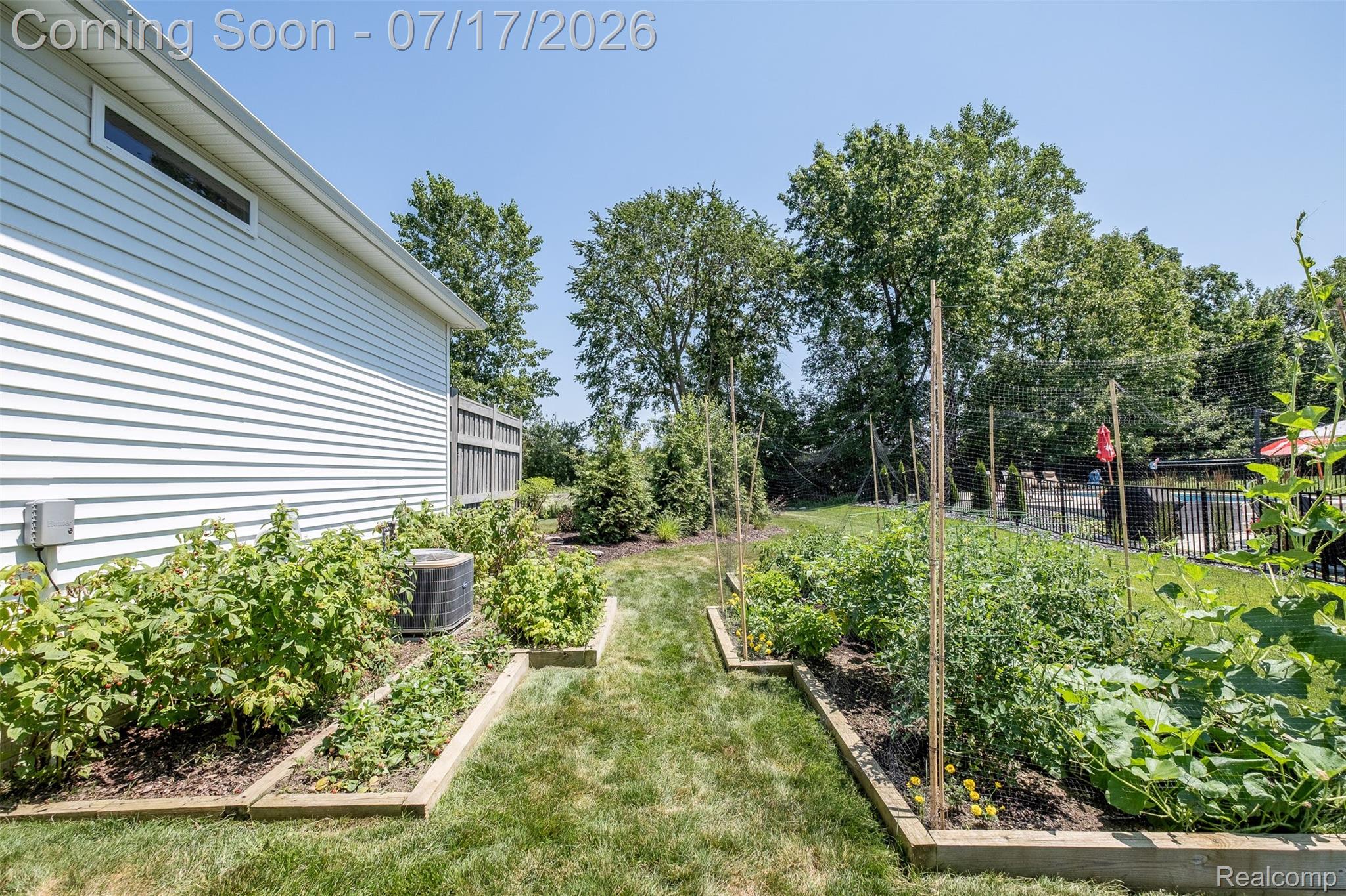 12349 Sugar Maple Drive Fenton, MI 48430 - Photo 61 of 67 Expansive backyard featuring multiple raised garden beds, established greenery, a white vinyl-sided exterior, a black metal fence, and mature trees