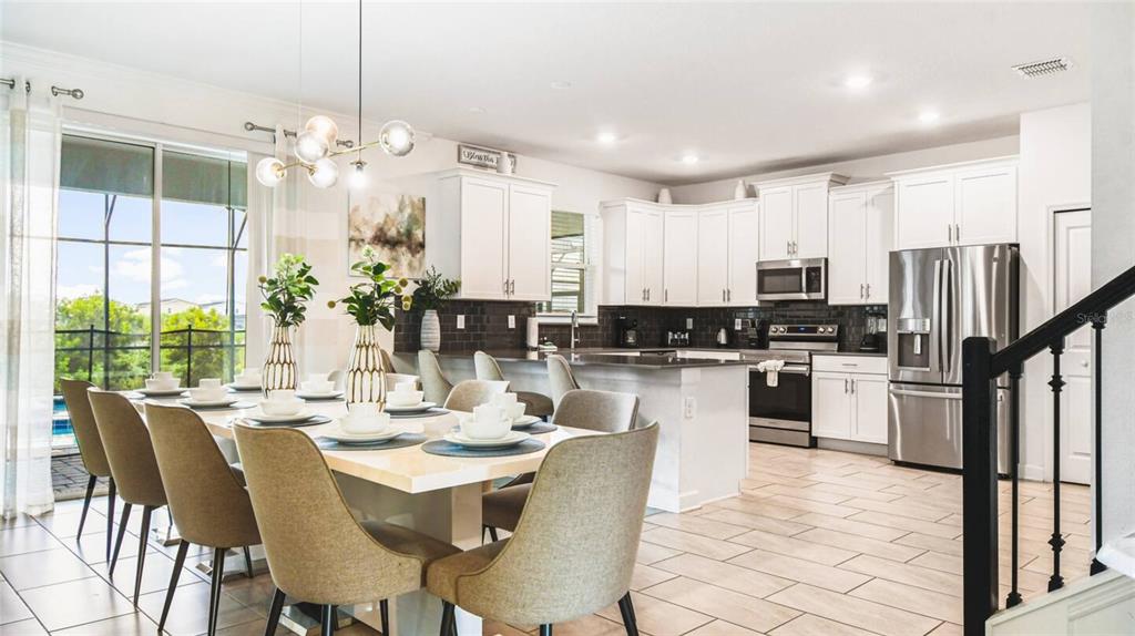 2916 Simile Street Kissimmee, FL 34746 - Photo 4 of 55 a kitchen with stainless steel appliances kitchen island granite countertop a dining table chairs and white cabinets