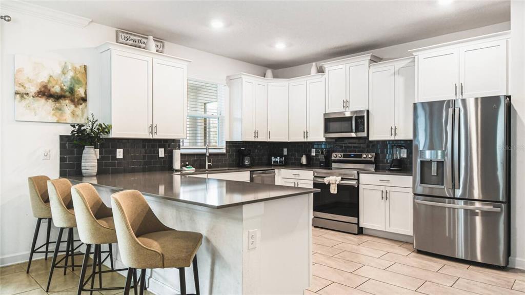 2916 Simile Street Kissimmee, FL 34746 - Photo 8 of 55 a kitchen with stainless steel appliances kitchen island granite countertop a table chairs microwave and sink