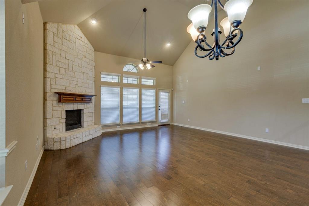 1522 Blue Jay Road Garland, TX 75043 - Photo 16 of 32 Spacious living area featuring a vaulted ceiling, wood-finish flooring, a stone-clad fireplace with a wood mantle, a decorative chandelier, and a wall of windows with blinds