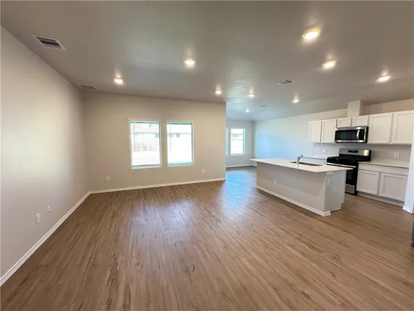an open kitchen with white cabinets wooden floor and a refrigerator