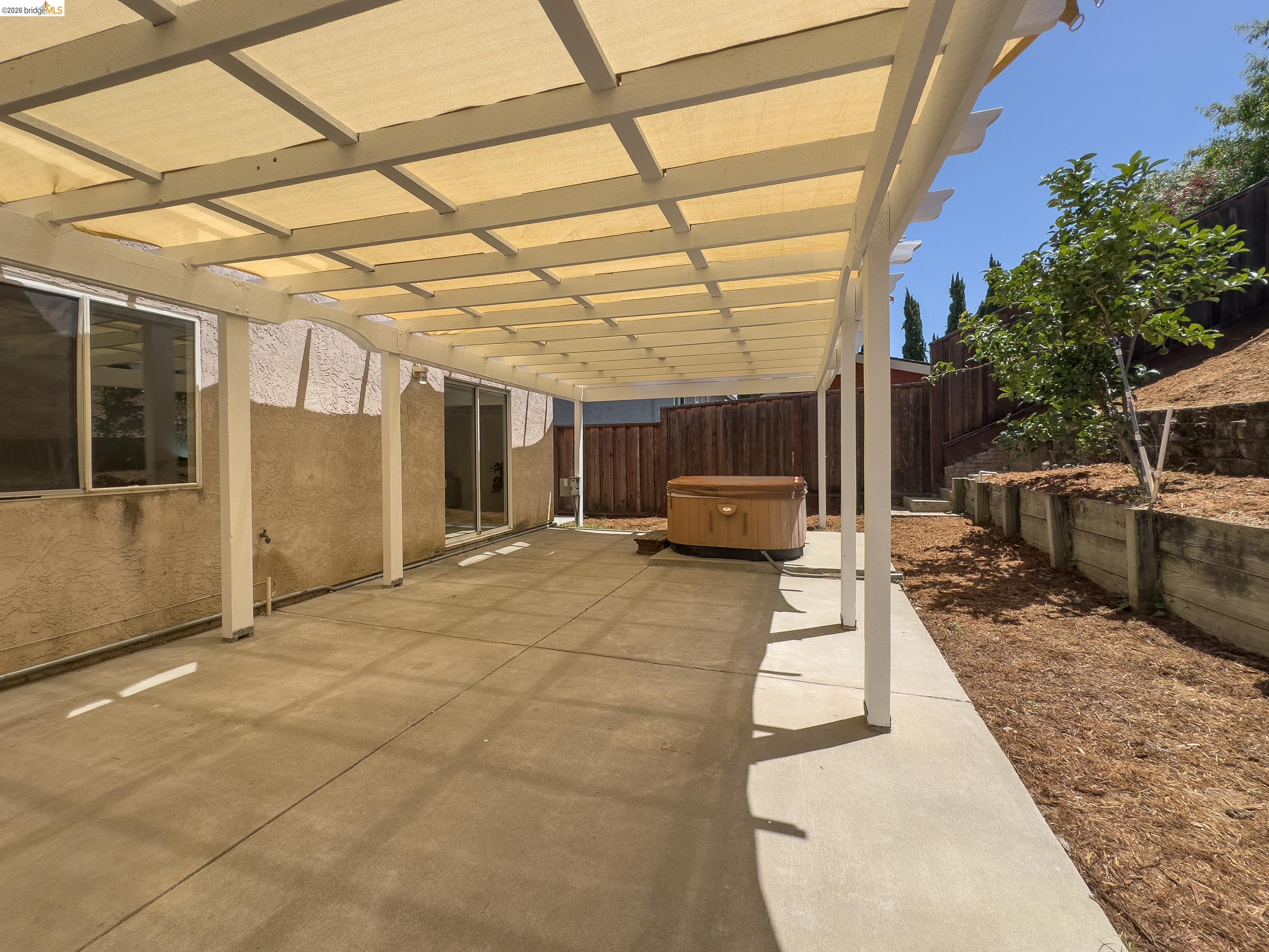512 Burdick Drive Bay Point, CA 94565 - Photo 37 of 50 Expansive concrete patio featuring a white pergola with a light-colored fabric shade, a built-in spa, and sliding glass doors accessing the interior