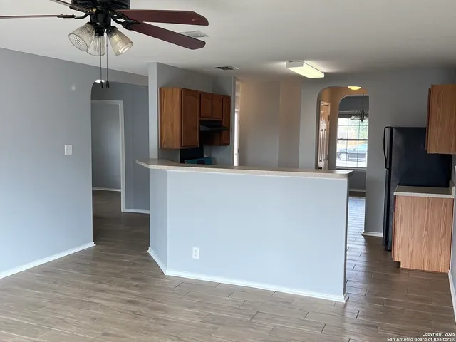 an empty room with wooden floor a chandelier fan and windows