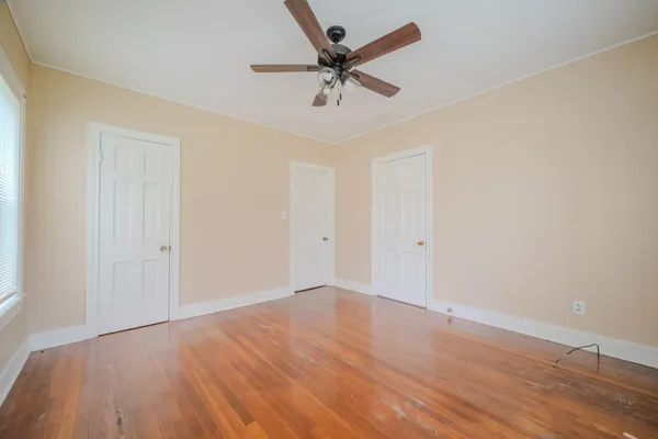 an empty room with wooden floor ceiling fan and windows