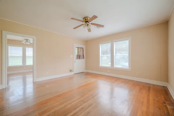 an empty room with wooden floor windows and fan