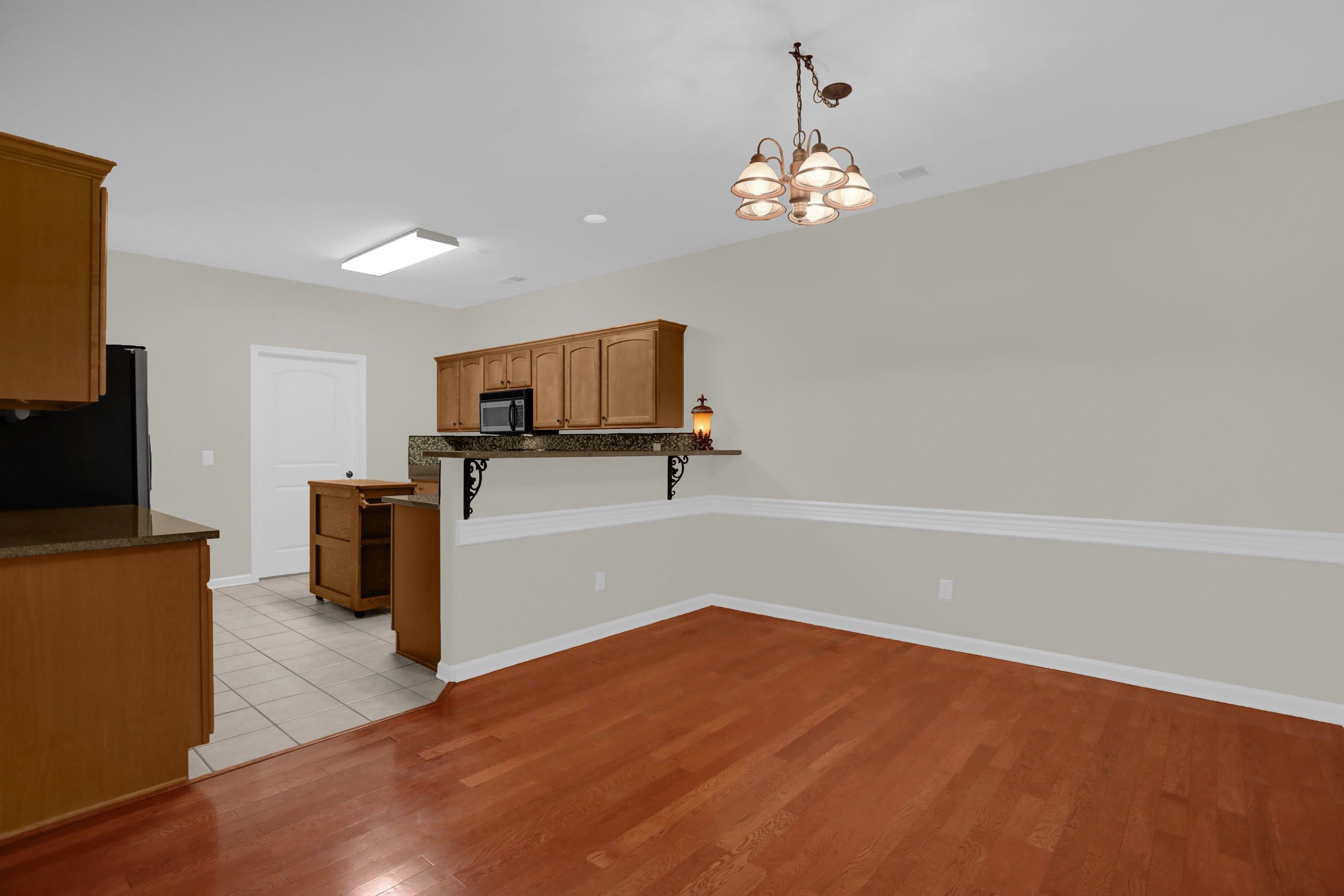 34 Peyton Ridge Drive, Unit 21 Collierville, TN 38017 - Photo 12 of 37 Kitchen and dining area featuring warm wood-finish flooring, a breakfast bar with decorative corbels, and overhead lighting