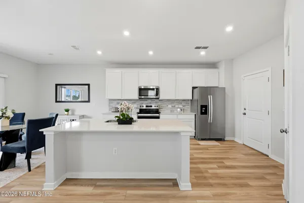 a large white kitchen with stainless steel appliances kitchen island a stove a refrigerator a table and chairs