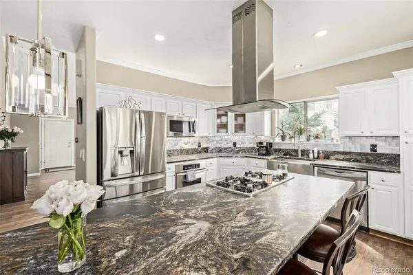 an open kitchen with granite countertop a stove a sink dishwasher a refrigerator and white cabinets with wooden floor