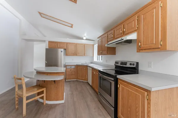 a kitchen with stainless steel appliances a stove a sink dishwasher and wooden cabinets with wooden floor