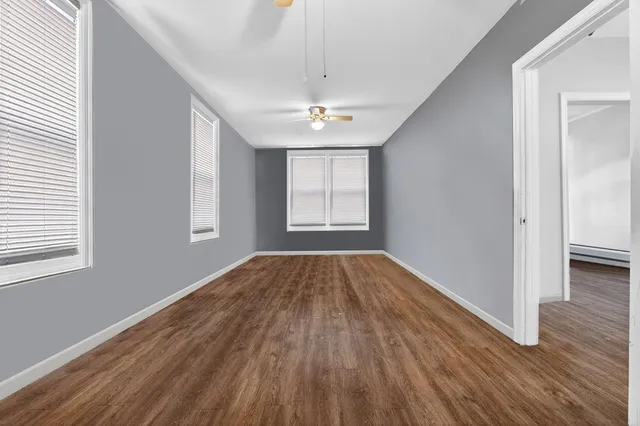 an empty room with wooden floor chandelier fan and windows