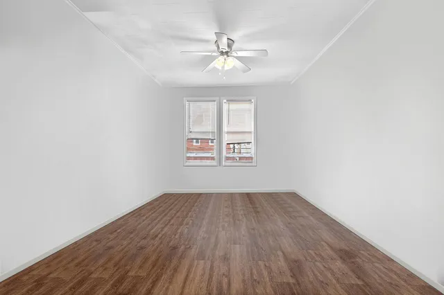 an empty room with wooden floor chandelier fan and windows