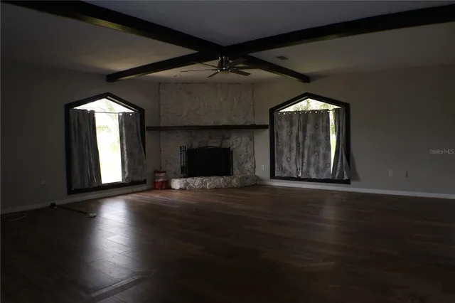 an empty room with wooden floor fireplace and windows