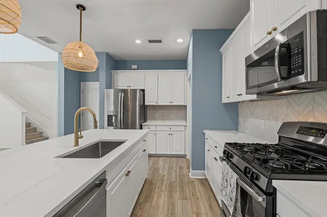 a kitchen with stainless steel appliances granite countertop a sink dishwasher a stove top oven a refrigerator with white cabinets and wooden floor