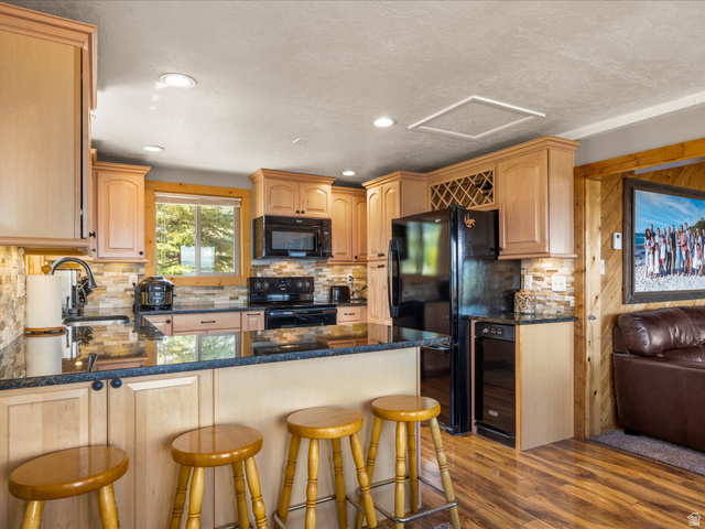 371 Lewis Loop, Unit 29 Fish Haven, ID 83287 - Photo 21 of 40 Kitchen featuring light wood cabinetry, black appliances, a stone tile backsplash, dark countertops, and wood-finish flooring