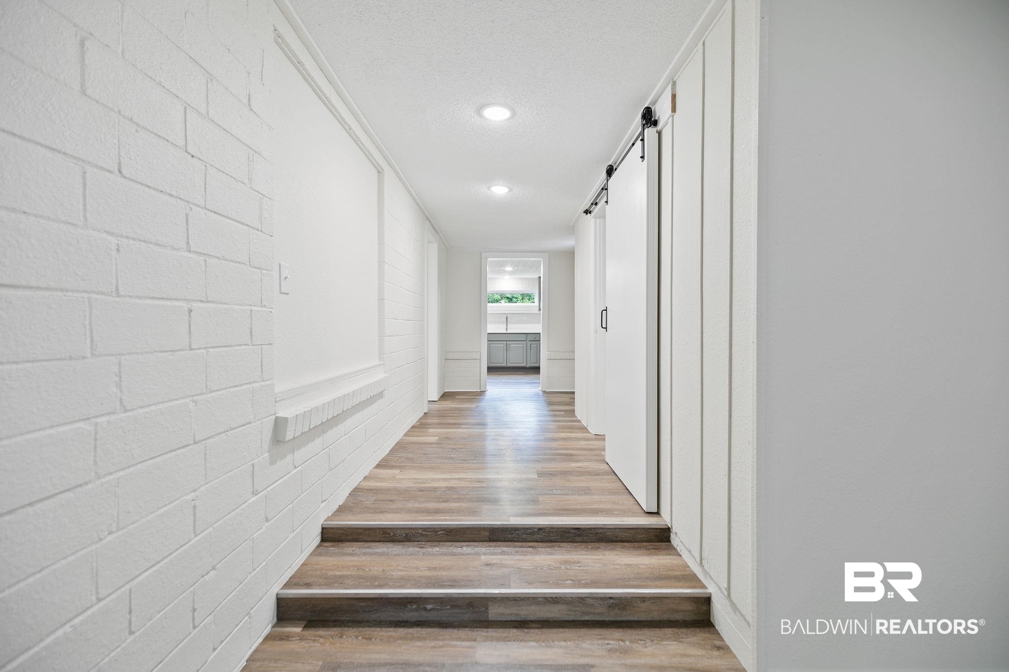 507 Byrne Street Bay Minette, AL 36507 - Photo 7 of 40 Hallway with brick wall, a textured ceiling, light hardwood / wood-style flooring, and a barn door