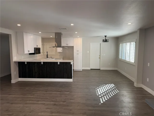 a hall with kitchen island granite countertop a sink and a wooden floor