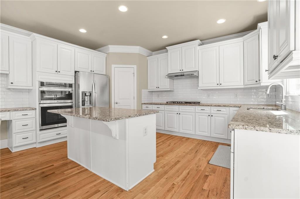 955 Gardiner Circle Suwanee, GA 30024 - Photo 12 of 44 a kitchen with kitchen island granite countertop a stove top oven a sink and white cabinets with wooden floor
