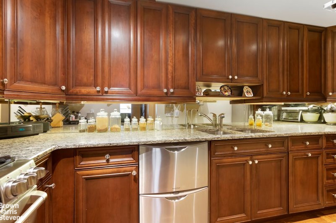 110 East 57th Street, Unit 4FG Manhattan, NY 10022 - Photo 6 of 9 a kitchen with granite countertop wooden cabinets a sink and dishwasher