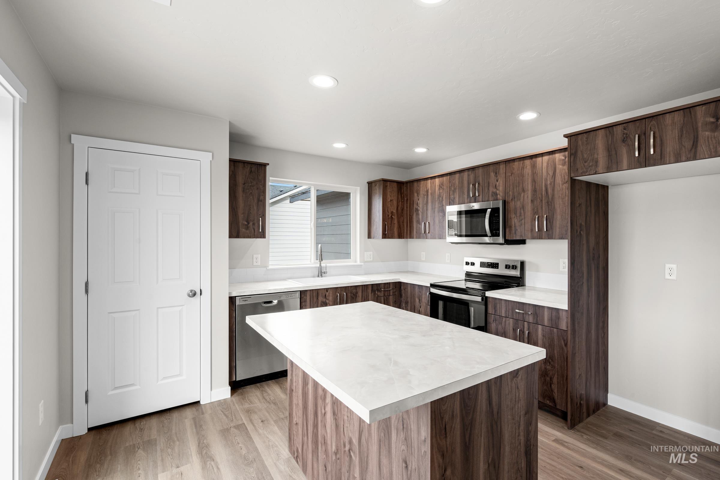 503 Hamlow Avenue Middleton, ID 83644 - Photo 4 of 21 Kitchen featuring stainless steel appliances, light countertops, dark wood finish cabinets, light wood finished floors, and a center island