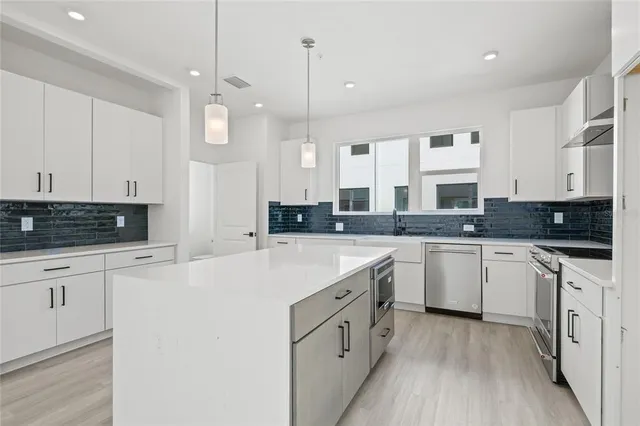 a large white kitchen with stainless steel appliances granite countertop a stove a sink dishwasher and white cabinets with wooden floor