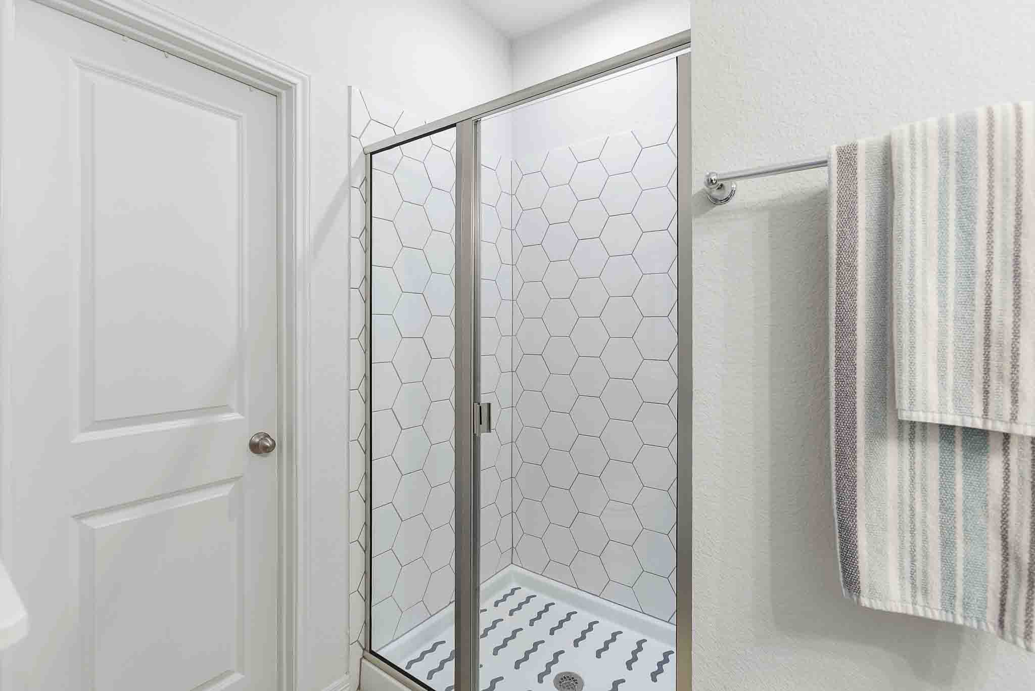 166 West Branch Road Kyle, TX 78640 - Photo 33 of 39 A well-lit shower features hexagonal tile work, creating a clean and geometric aesthetic.