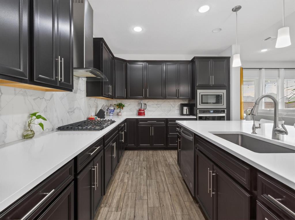636 Corner Post Path Celina, TX 75009 - Photo 11 of 40 Contemporary kitchen featuring dark wood cabinetry, white countertops, marble-look backsplash, stainless steel appliances, and wood-finish flooring