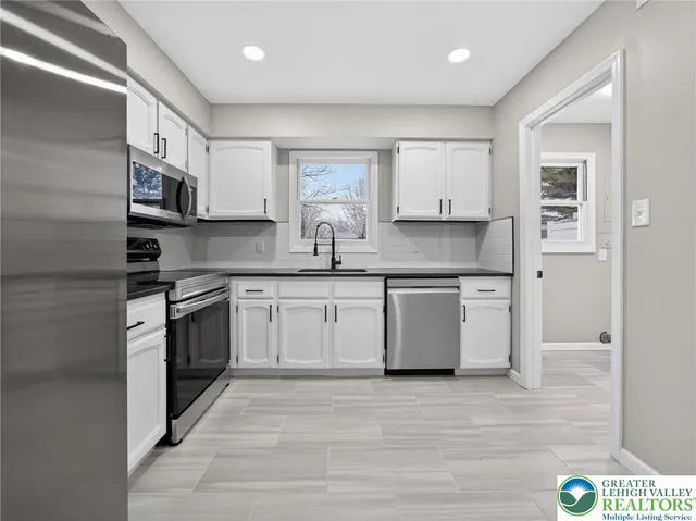 a kitchen with stainless steel appliances granite countertop a sink a stove a refrigerator and white cabinets