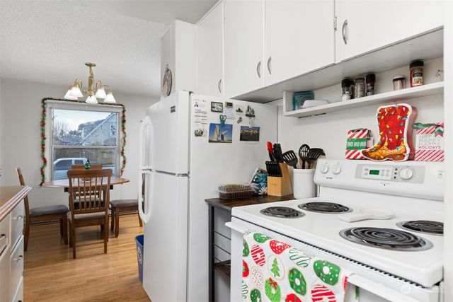 a white kitchen with a refrigerator a stove a dining table and chairs with wooden floor