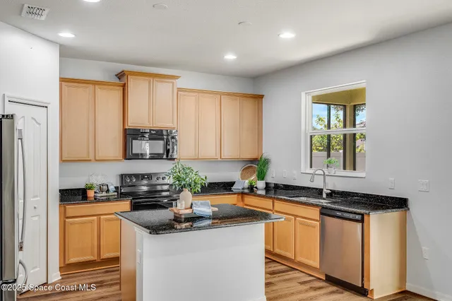a kitchen with stainless steel appliances granite countertop a sink a stove a refrigerator cabinets and a window
