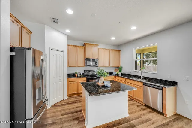 a kitchen with granite countertop a refrigerator a stove a sink dishwasher and wooden cabinets with wooden floor