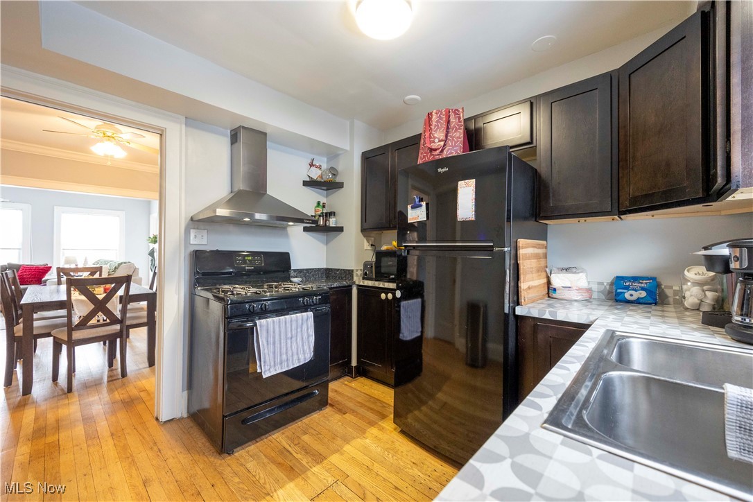 2075 Coventry Road Cleveland, OH 44118 - Photo 19 of 41 Kitchen with sink, wall chimney exhaust hood, light hardwood / wood-style flooring, dark brown cabinets, and black appliances