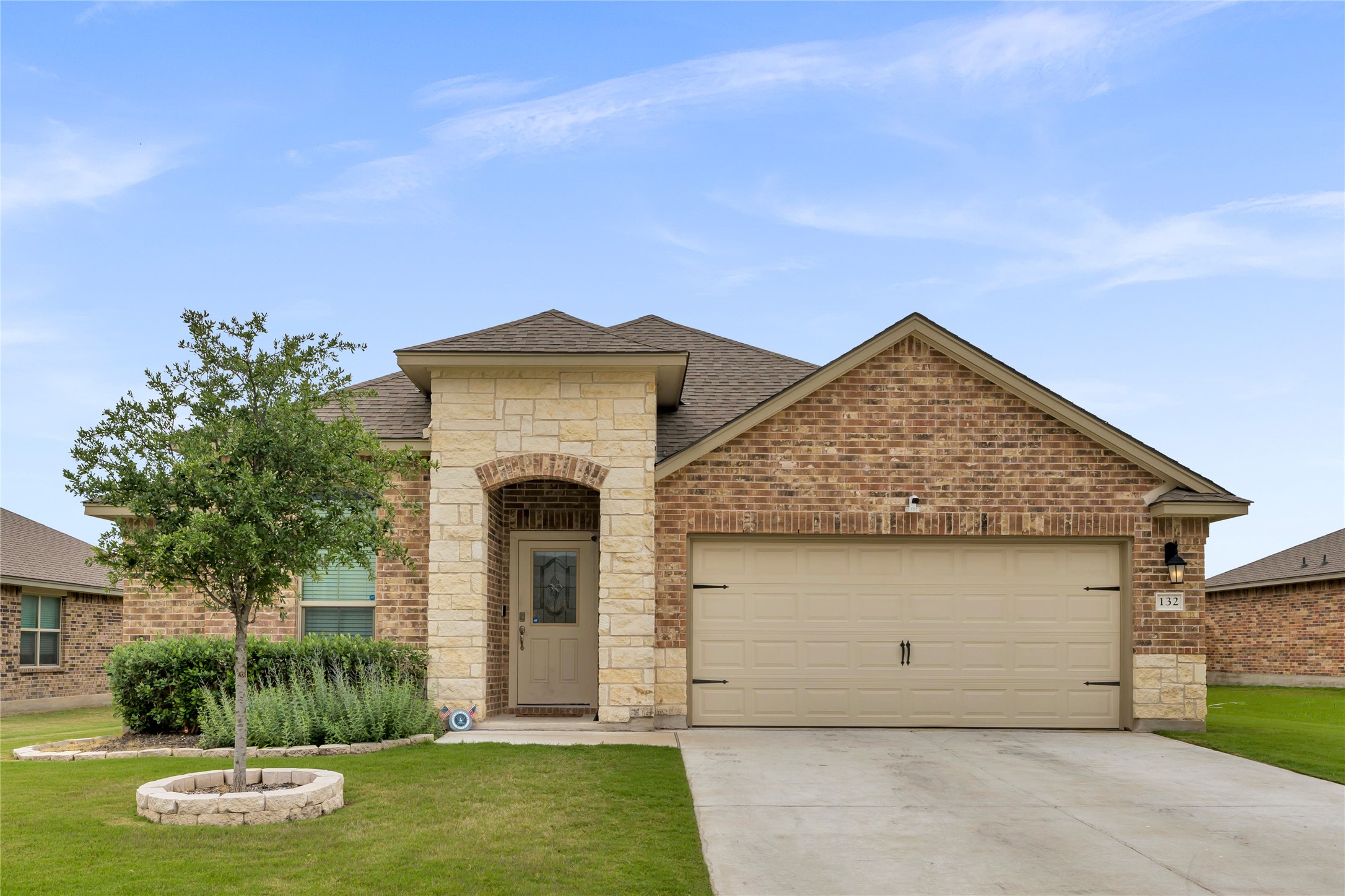 132 Cinnamon Loop Burnet, TX 78611 - Photo 1 of 27 Brick and stone facade featuring an arched entry, an attached two-car garage, and a manicured lawn