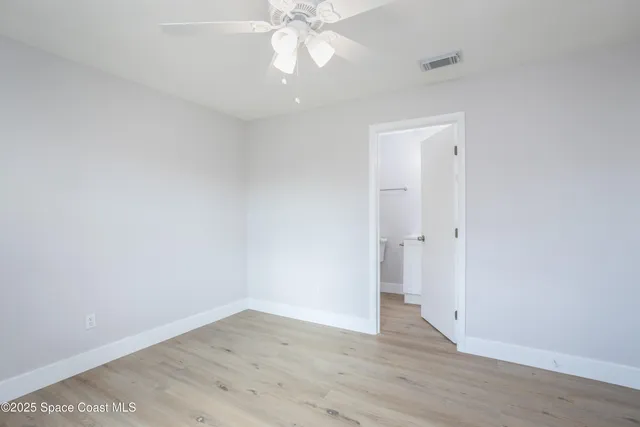 a view of an empty room with wooden floor and a ceiling fan