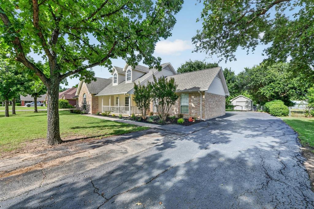 421 Ben Boyd Road Argyle, TX 76226 - Photo 4 of 25 Traditional-style home featuring a brick facade, dormer windows, a covered front porch with white railings, mature trees, and an asphalt driveway leading to a detached shed