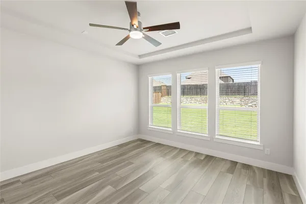 an empty room with wooden floor fan and windows