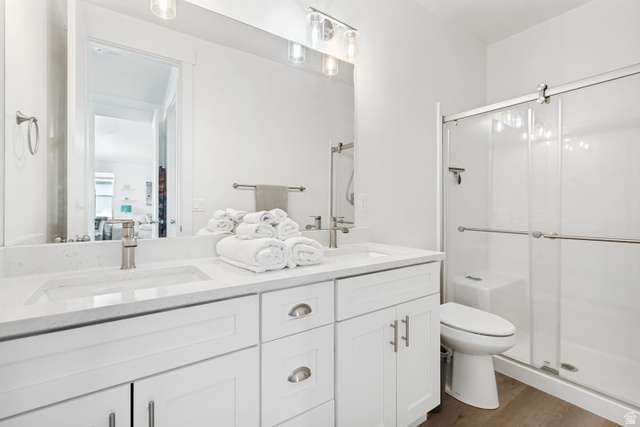 683 Kings Landing Tooele, UT 84074 - Photo 18 of 39 Contemporary bathroom featuring a double vanity with stone countertops and undermount sinks, white cabinetry with brushed nickel hardware, a spacious walk-in shower with a glass enclosure, and wood-finish flooring
