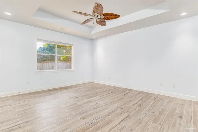 an empty room with wooden floor chandelier fan and windows
