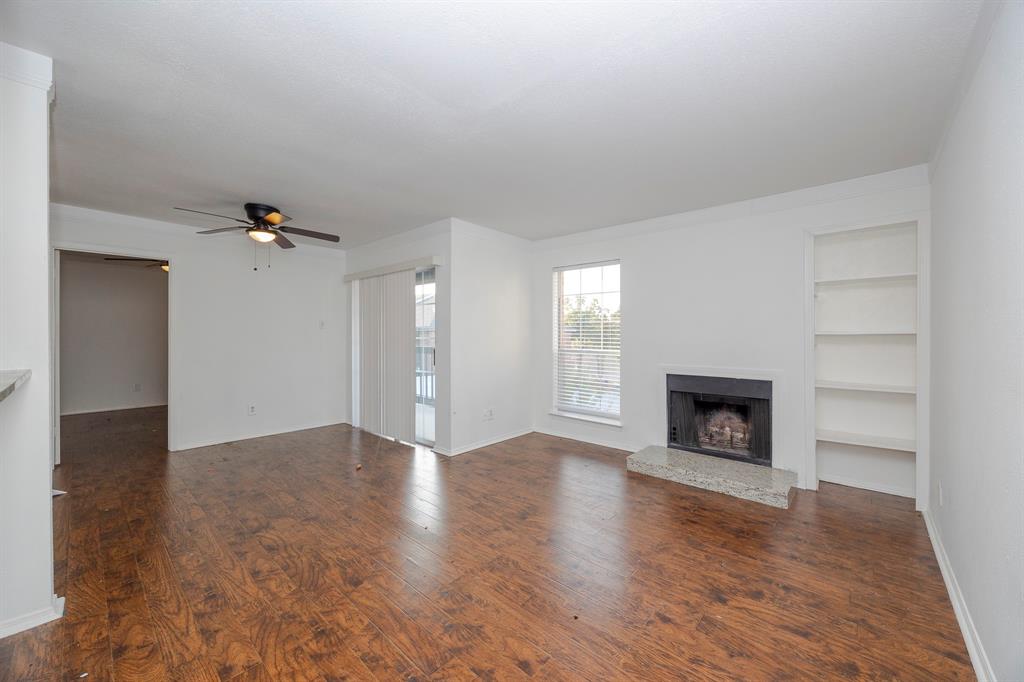 18333 Roehampton Drive, Unit 825 Dallas, TX 75252 - Photo 2 of 23 Wood-finish flooring, built-in shelving, fireplace with stone hearth, sliding glass door, and ceiling fan
