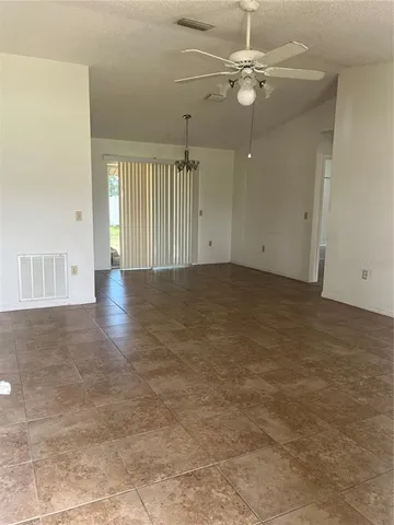 an empty room with chandelier fan and windows